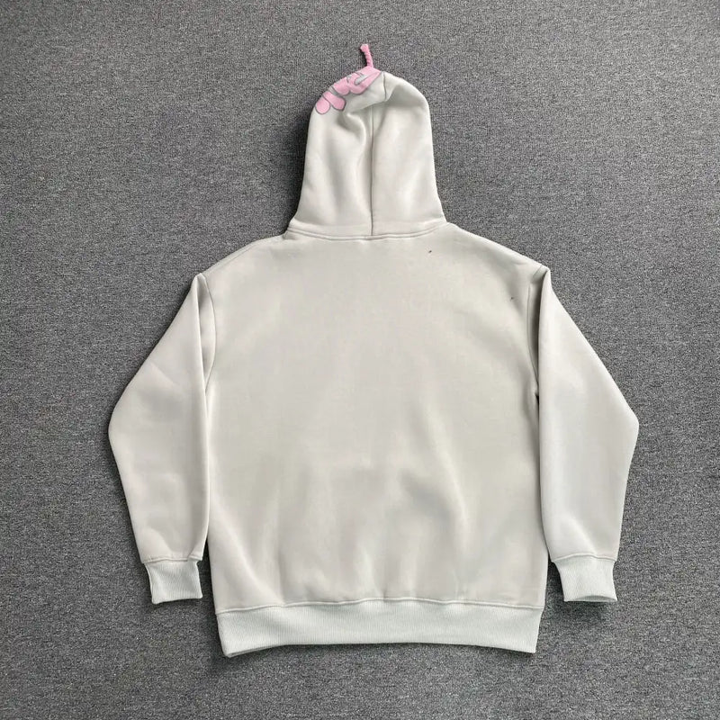 The Syna World Grey Pink Graphic Hood Oversized Hoodie is shown laid flat, back view on a gray surface. Its hood displays a small pink graffiti-style graphic resembling three fingers—an eye-catching streetwear detail.