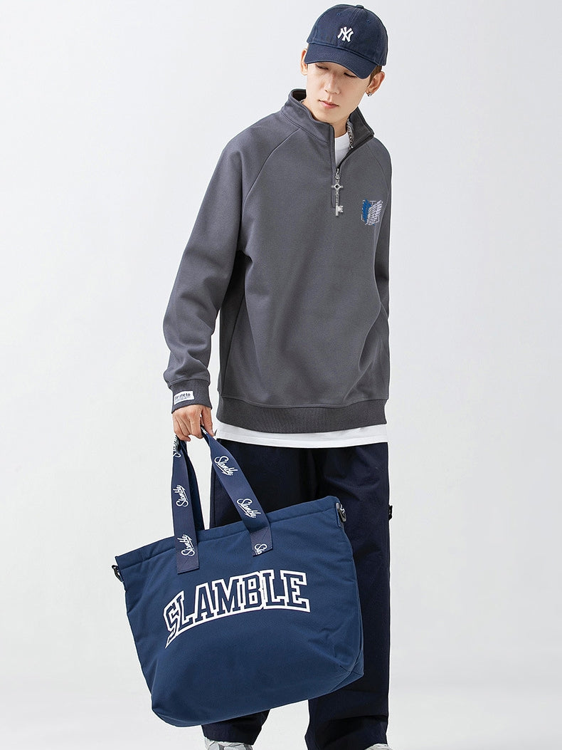 A person in a dark cap, gray Limited Edition Attack on Titan Half-Zip Sweatshirt featuring Eren’s Key Zipper and Scout Regiment Logo, and dark pants holds a large blue SLAMBLE bag against a plain backdrop for a minimalist look.