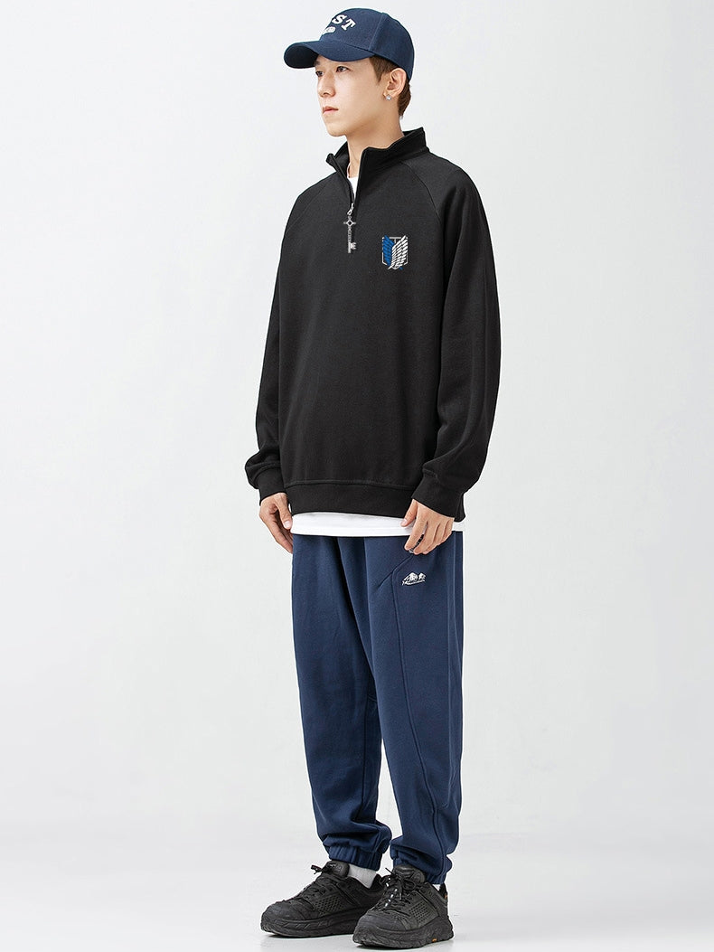 A person wearing an Attack on Titan Limited Edition Half-Zip Sweatshirt with Eren's Key zipper, a blue cap, blue sweatpants, and black sneakers stands against a white background. Their hands are in their pockets, and they are looking to their right.